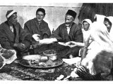 Bokhara Jews in Jerusalem gather to share the Passover Feast. The unleavened bread is handed round and in the middle we see the wine and the `bitter herbs`. An early photograph.